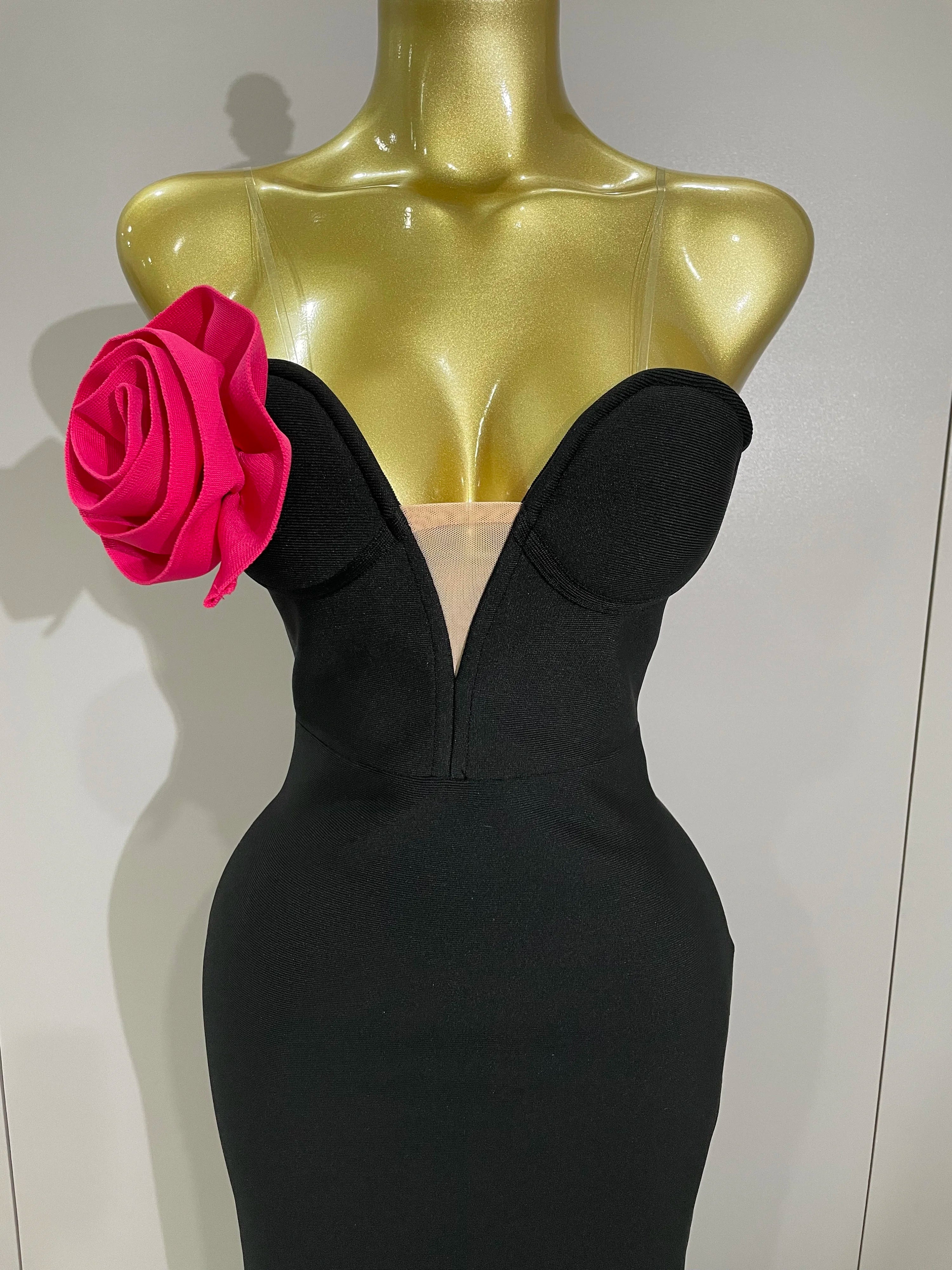 Black evening gown with a pink rose on a mannequin against a white background