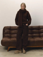 Person wearing a brown outfit standing in front of a brown sofa against a plain wall.