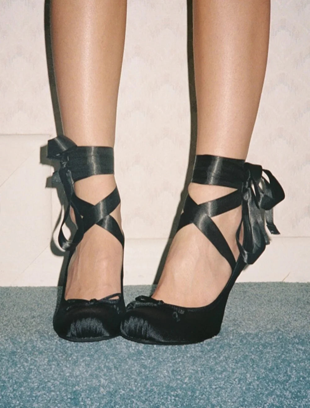 Black high-heeled shoes with bow details on a neutral background