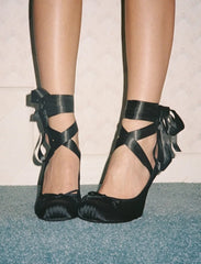 Black high-heeled shoes with bow details on a neutral background