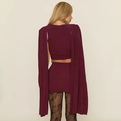 Woman wearing a burgundy outfit with a cape on a beige background