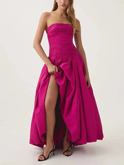 Woman wearing a strapless pink gown with a high slit on a white background