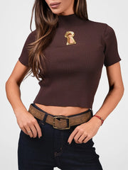 Woman wearing a brown ribbed crop top with a gold brooch and dark jeans on a white background