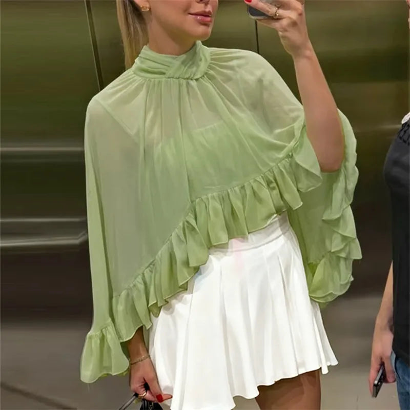 Woman wearing a light green blouse with ruffled details and a white skirt.