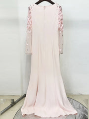 Pink dress with floral embellishments on a hanger against a white wall.