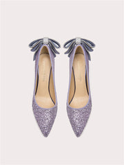 Pair of glittery purple high heels with bow details on a light gray background