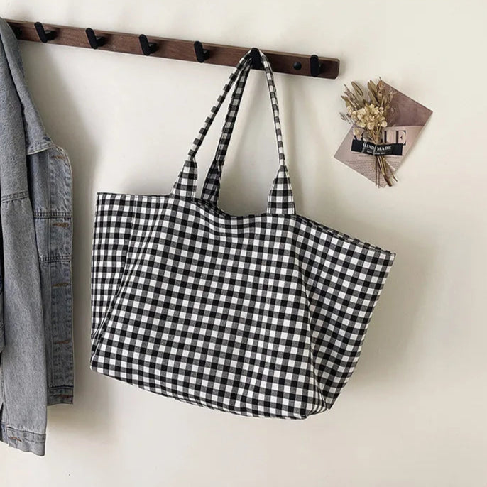 Black and white checkered bag hanging on a wooden rack with a denim jacket and a small bouquet of flowers in the background.
