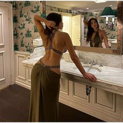 Woman in a green dress standing in a bathroom looking at herself in the mirror.