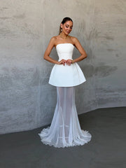 Woman wearing a strapless white dress with sheer overlay against a plain background
