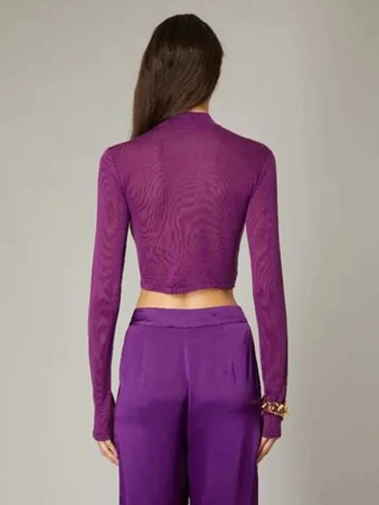 Person wearing a purple outfit with long sleeves and high waist pants on a plain background
