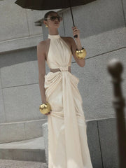 Woman in a flowing beige dress holding an umbrella against a gray stone wall.