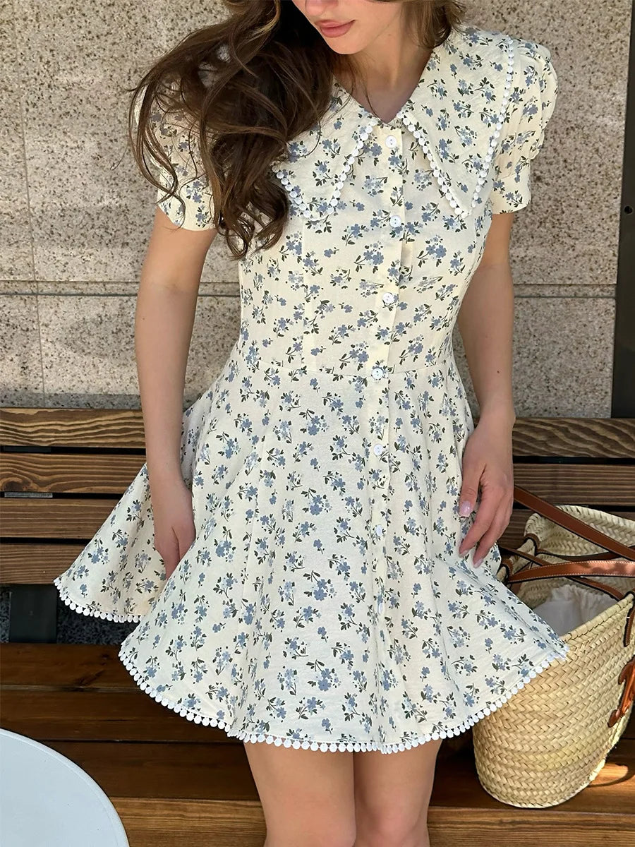 Woman wearing a floral dress standing outdoors with a textured wall background