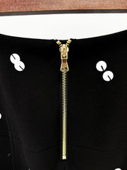 Close-up of a black garment with a gold zipper and white buttons.