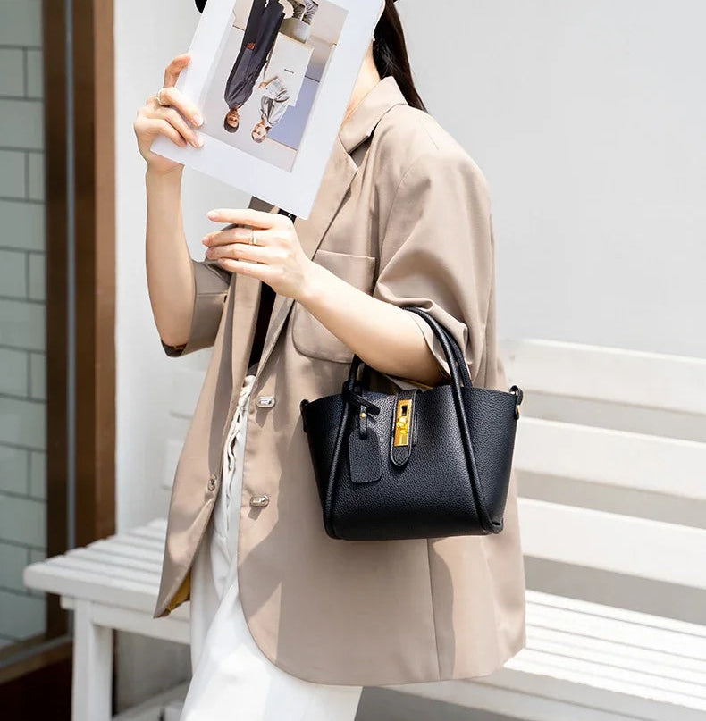 Person holding a black handbag and a photo album outdoors on a bench.