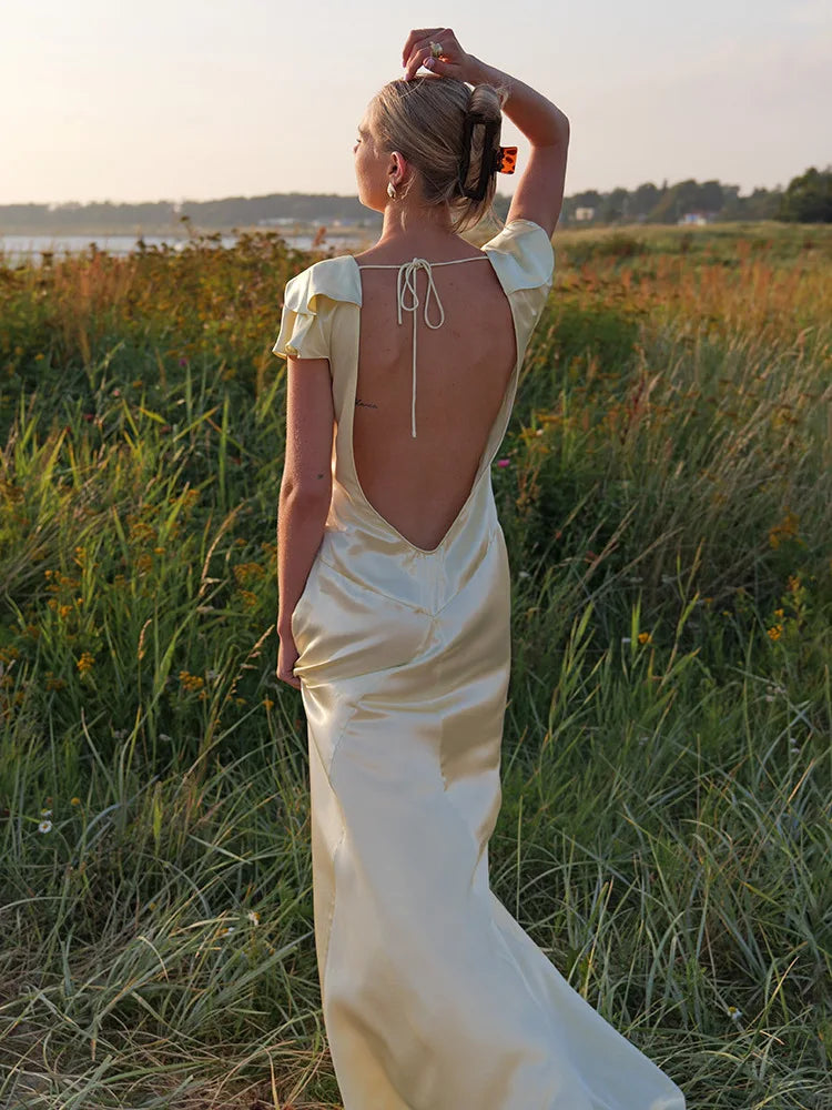 Woman in a flowing dress standing in a field with a sunset background