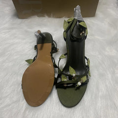 Green high-heeled sandals with decorative straps on a white surface