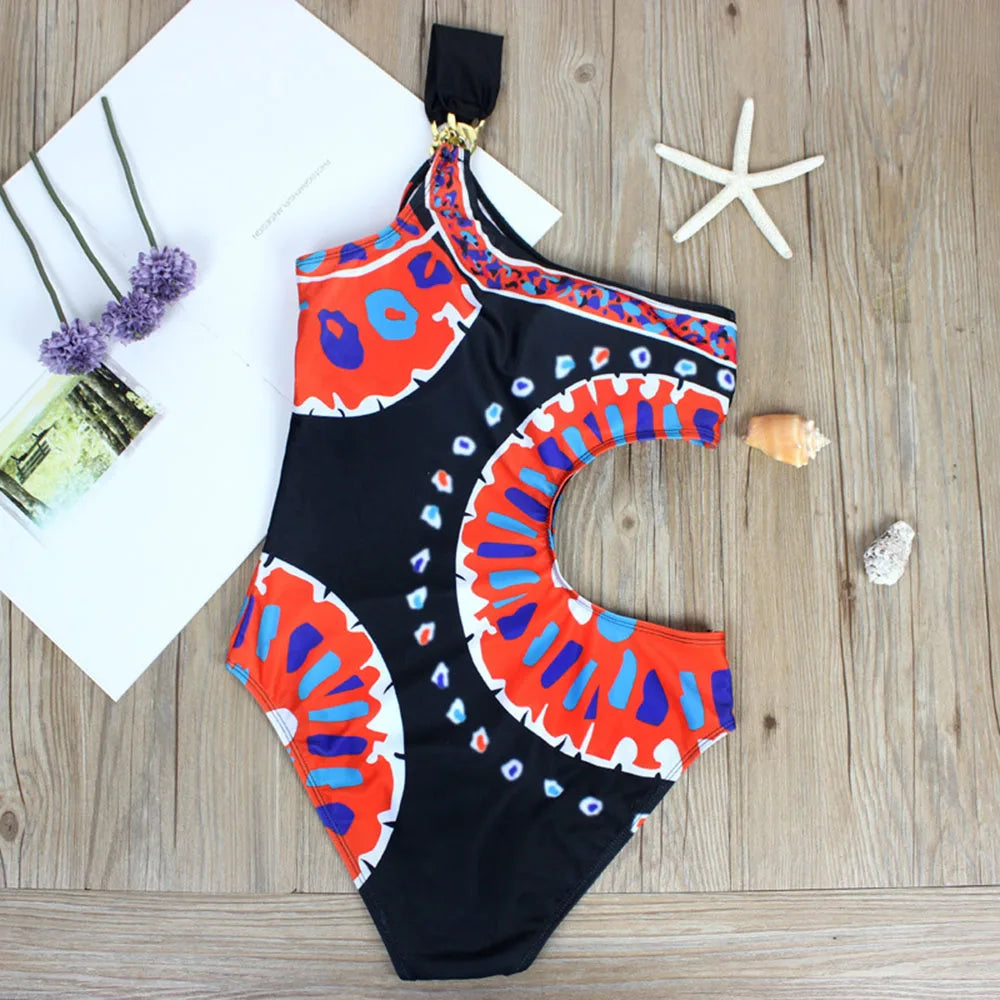 Flat lay of a one-piece swimsuit with a one-shoulder design and a graphic pattern, styled with beach accessories.