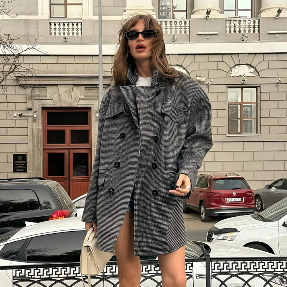 Woman in a gray coat standing on a city street with cars and buildings in the background