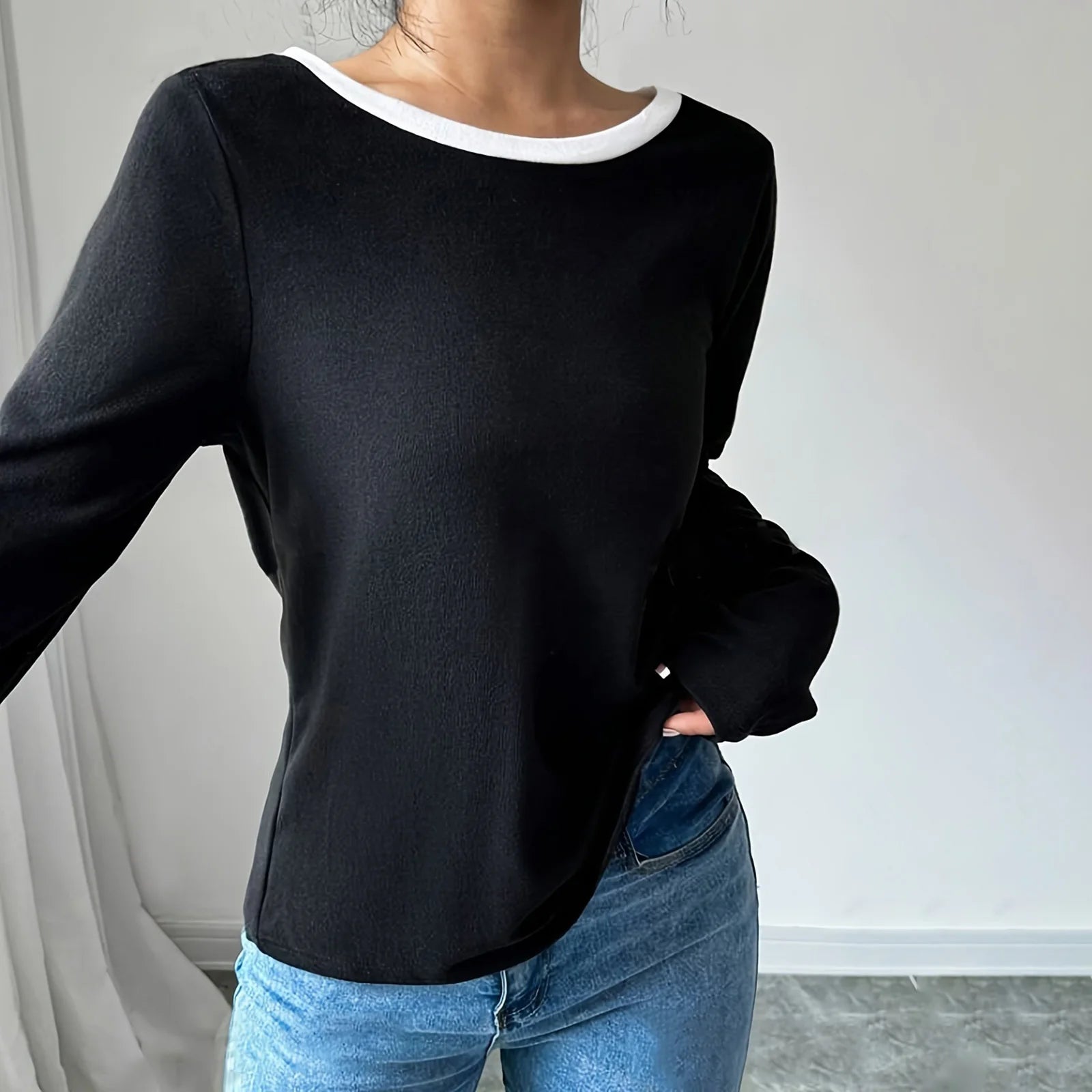 Person wearing a black long-sleeve top and blue jeans against a neutral background