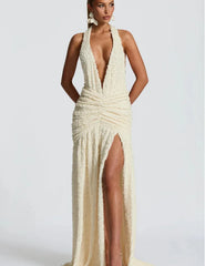 Woman wearing a white evening gown with a deep neckline and high slit on a plain background