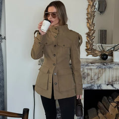 Woman in a beige coat drinking from a coffee cup in a room with decorative elements.