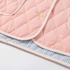 Pink quilted baby blanket with a button on a light gray background