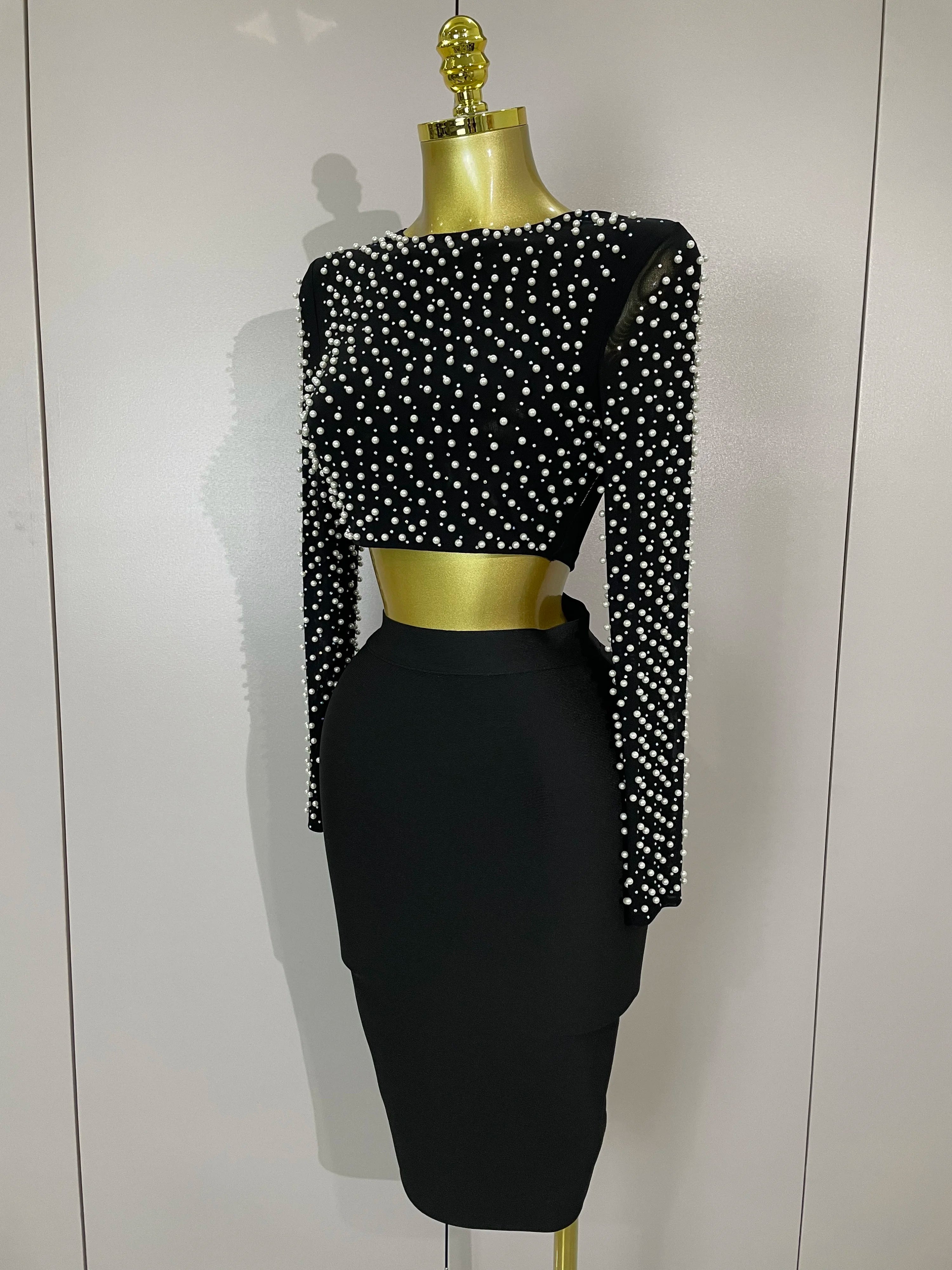 Black pearl embelished top and skirt set with long sleeves on a mannequin against a white background.