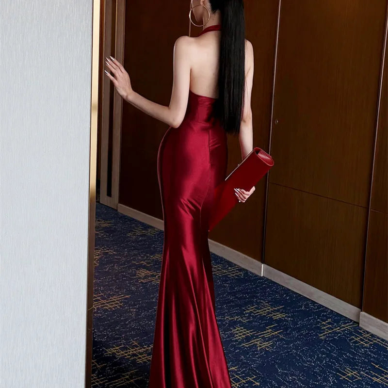 Woman in a red satin dress holding a clutch, standing in a room with blue carpet.