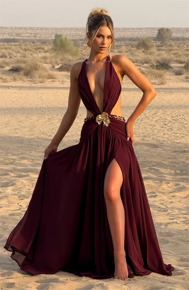 Woman in a burgundy evening gown with a high slit standing in a desert landscape.