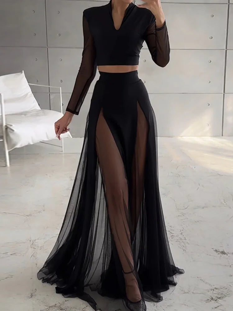 Black two-piece outfit with sheer long sleeves and high slit skirt on a neutral background