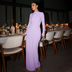 Woman in a lavender dress standing in a dimly lit dining area with tables and chairs.