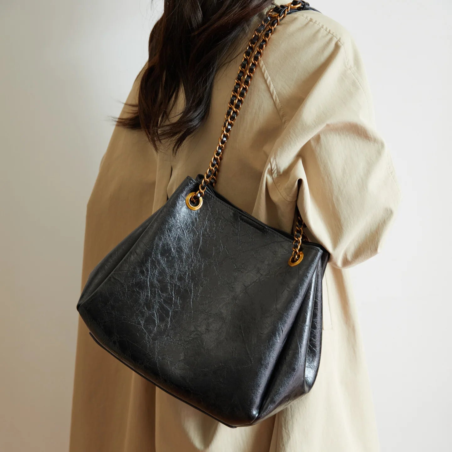 Person wearing a beige outfit with a black handbag featuring a gold chain strap.