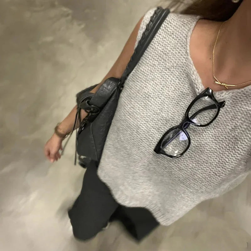 Person wearing a textured white top with a black bag and glasses on a neutral background