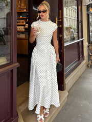 Woman in a white polka dot dress standing outside a store.