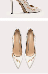 White high-heeled shoes with floral embroidery on a light gray background