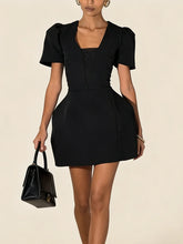 Woman wearing a black dress holding a matching handbag on a beige background