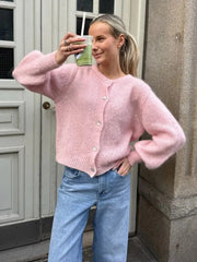 Woman wearing a pink cardigan and blue jeans, standing outside a building.