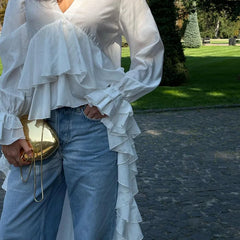 Person wearing a white ruffled blouse and blue jeans outdoors.
