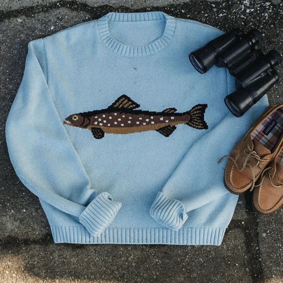 Light blue sweater with fish design, binoculars, and shoes on a textured surface