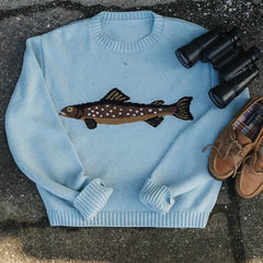 Light blue sweater with fish design, binoculars, and shoes on a textured surface