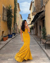 Woman in a yellow dress walking down a sunlit street with buildings and plants.