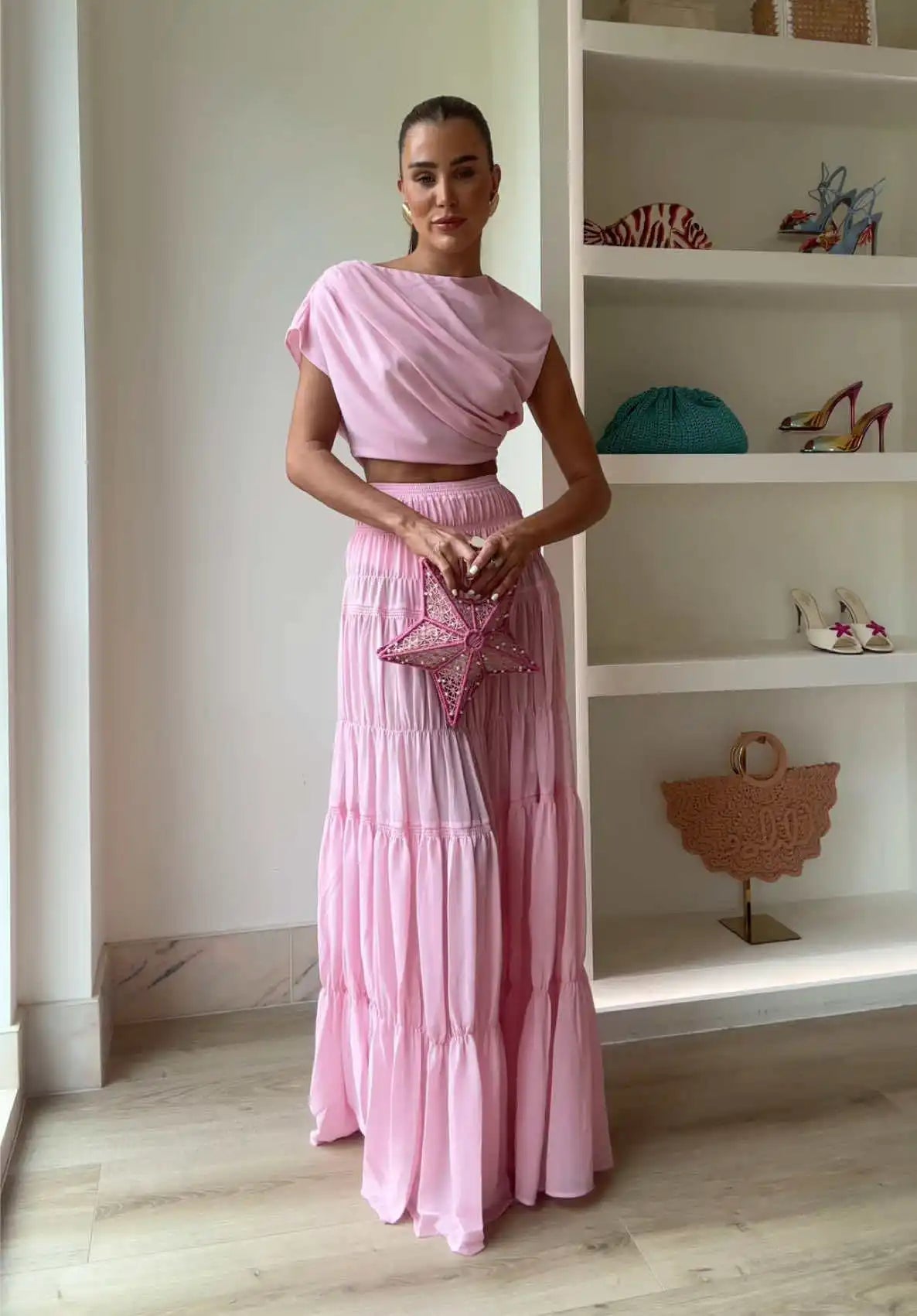Woman in a pink outfit standing in a room with shelves displaying various items.