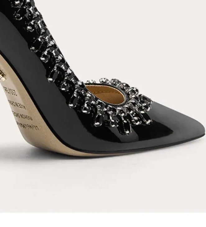 Black high-heeled shoe with embellishments on a light gray background