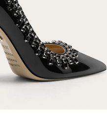 Black high-heeled shoe with embellishments on a light gray background