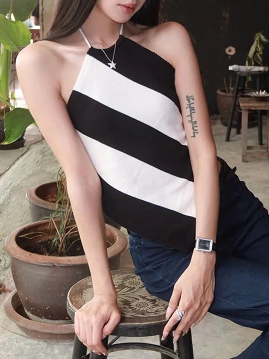 Woman wearing a black and white striped sleeveless top with a tattoo on her arm, sitting outdoors.