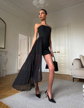 Woman in a black dress standing in a room with white walls and wooden floors.