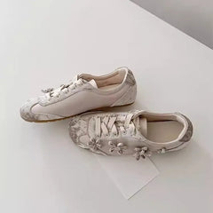 Pair of light grey sneakers with floral appliqu�s, shown from a side angle.