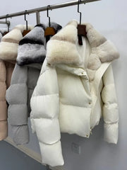 White puffer jacket with fur trim hanging on a rack against a white wall.