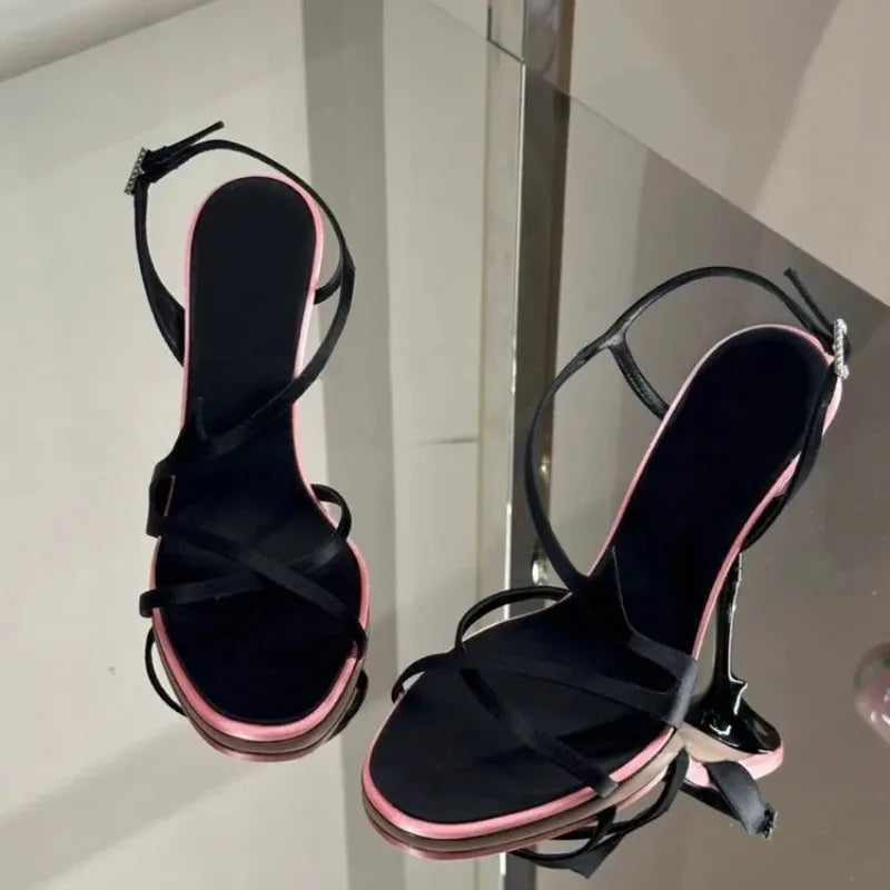 Black stiletto sandals with delicate straps on a mirrored surface
