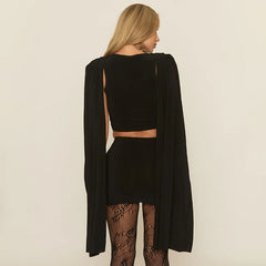 Person wearing a black outfit with a cape on a beige background